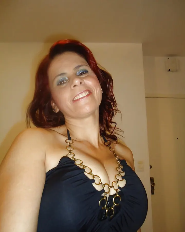 Femme aux cheveux roux, en robe noire, assise sur un fauteuil, regardant vers l'appareil, avec un maquillage naturel.