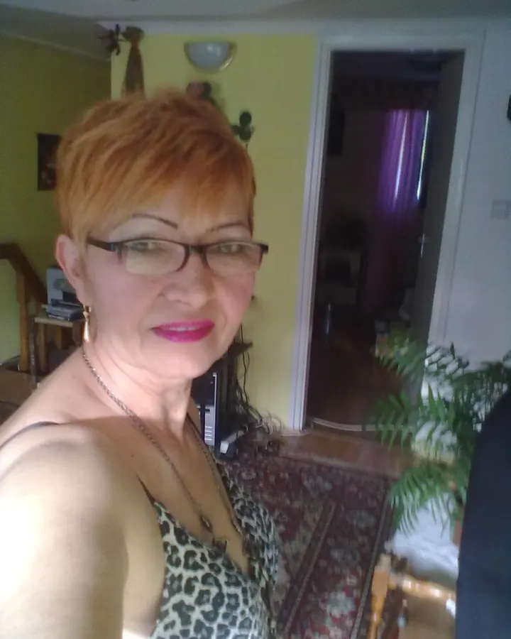 Femme aux cheveux roux, portant un haut noir, posant de face avec les bras levés, montrant des tatouages colorés.