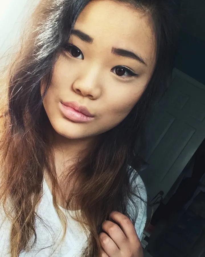 Femme asiatique aux cheveux longs et ondulés, regardant l'appareil photo dans une chambre.