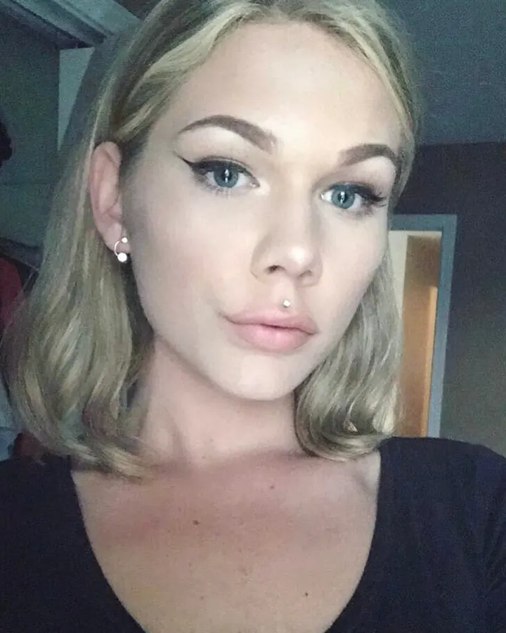 Jeune femme blonde aux yeux bleus, regard intense et direct vers l'objectif, lumière naturelle