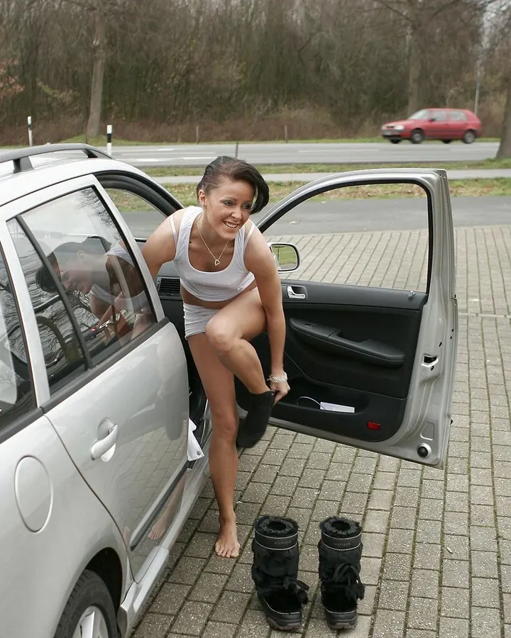 Femme en haut blanc et shorts blancs, sortant d'une voiture blanche, sourire, bottes noires à côté