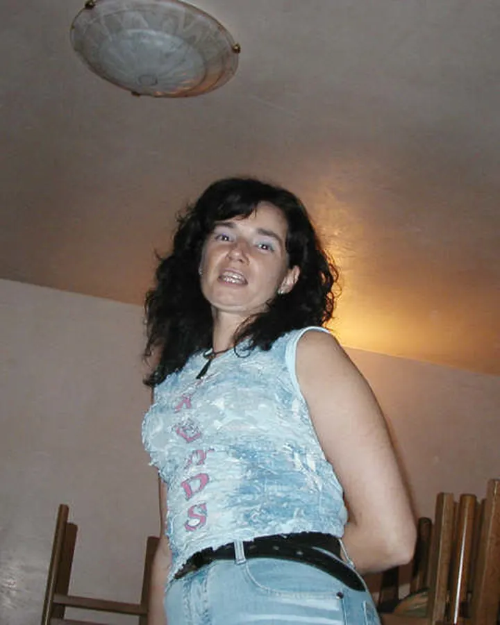 Femme aux cheveux foncés en débardeur bleu et jeans, dans une pièce éclairée par une lumière chaude