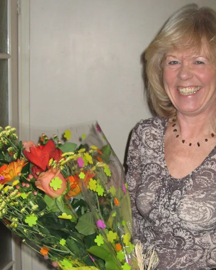 Femme européenne aux cheveux blancs, souriante, tenant un bouquet de fleurs colorées.
