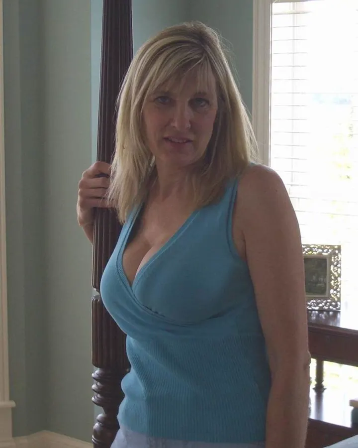 Femme blonde en haut turquoise, posant près d'une rampe en bois, regardant l'appareil photo.