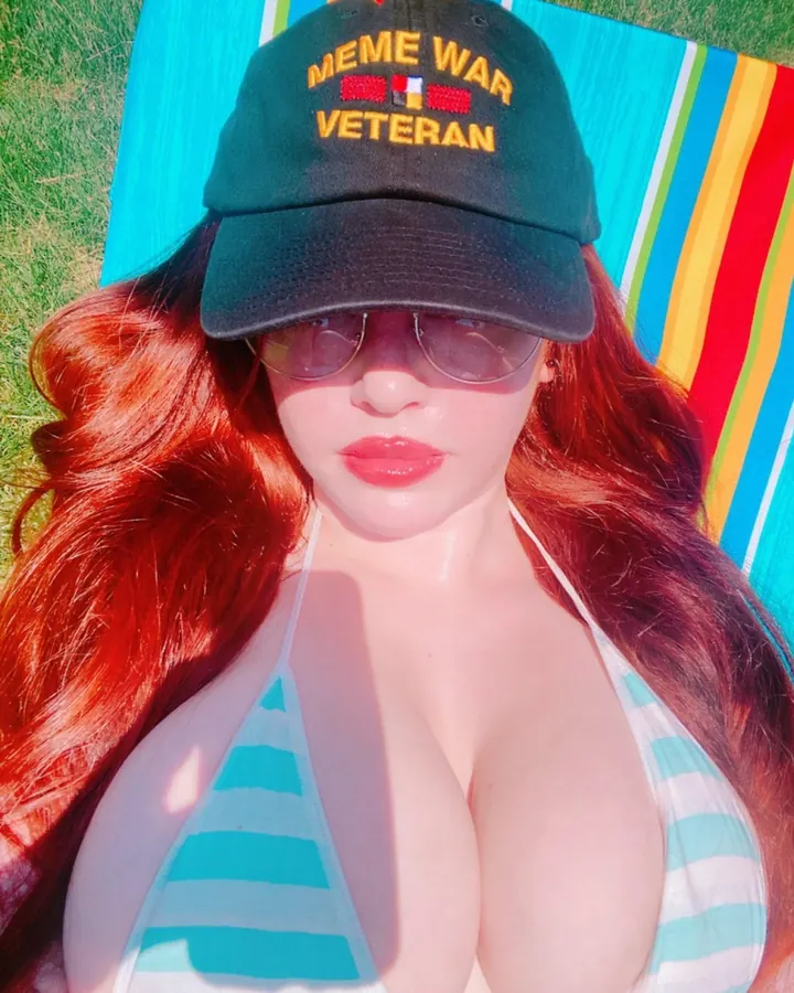 Femme en bikini rayé, allongée sur une serviette colorée, portant une casquette et des lunettes de soleil.