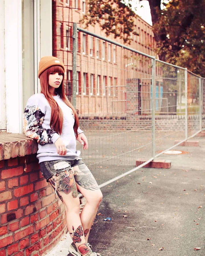 Femme en photo selfie, cheveux roux, regardant l'appareil, tatouage visible sur l'épaule.