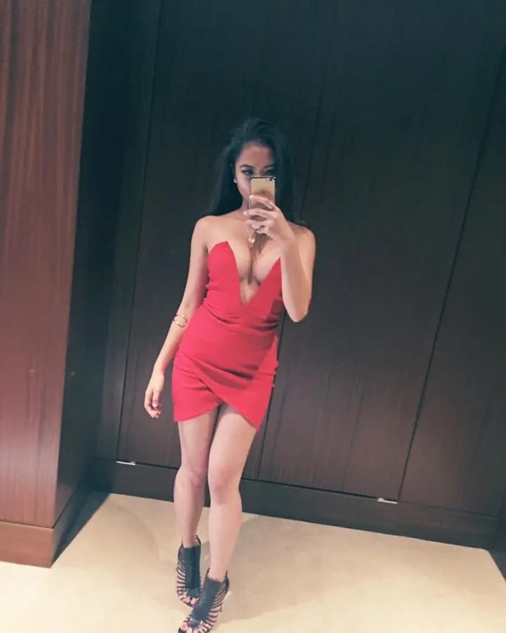 Femme en robe rouge ajustée, prenant un selfie dans un miroir, pieds nus.