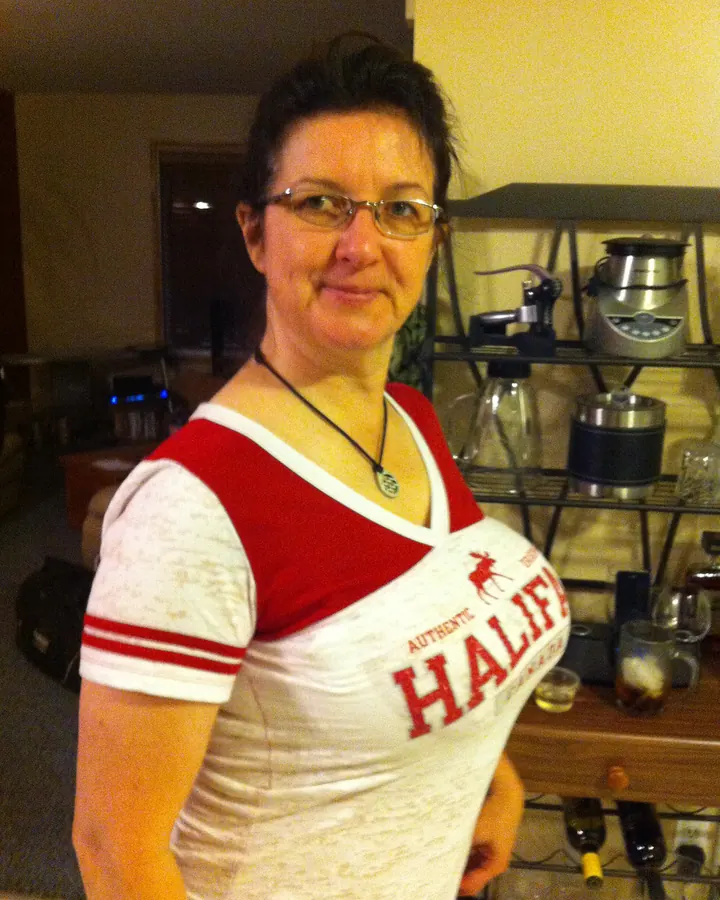 Femme aux cheveux bruns-noirs, lunettes, en t-shirt rouge et blanc, dans une pièce avec des objets de cuisine.